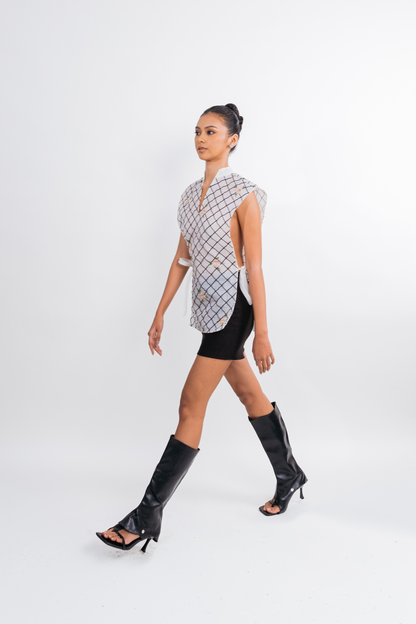 A model walks across a white studio background wearing a sleeveless black and white checkered vest, a black mini skirt, and black knee-high heeled sandals.