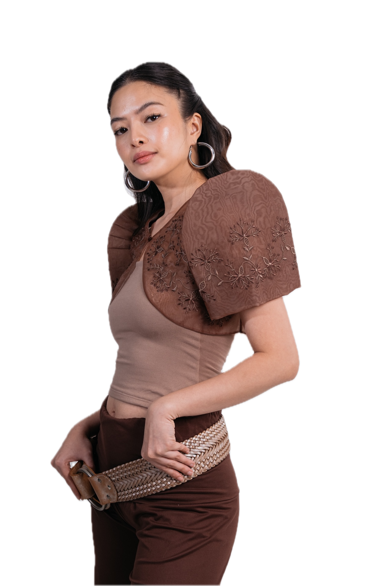 A woman modeling a brown sheer embroidered puff-sleeve shrug or cape over a beige top, paired with brown pants and a woven belt, against a solid white background.