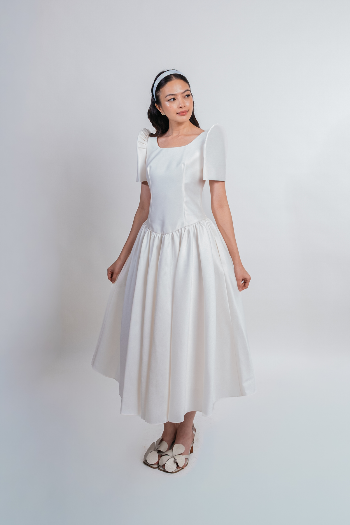 A woman modeling a white midi dress with butterfly sleeves, a square neckline, and a flared skirt, standing against a plain light gray studio background.
