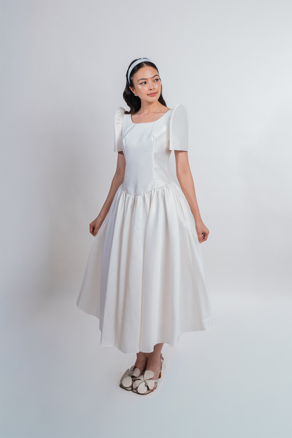 A woman modeling a white midi dress with butterfly sleeves, a square neckline, and a flared skirt, standing against a plain light gray studio background.