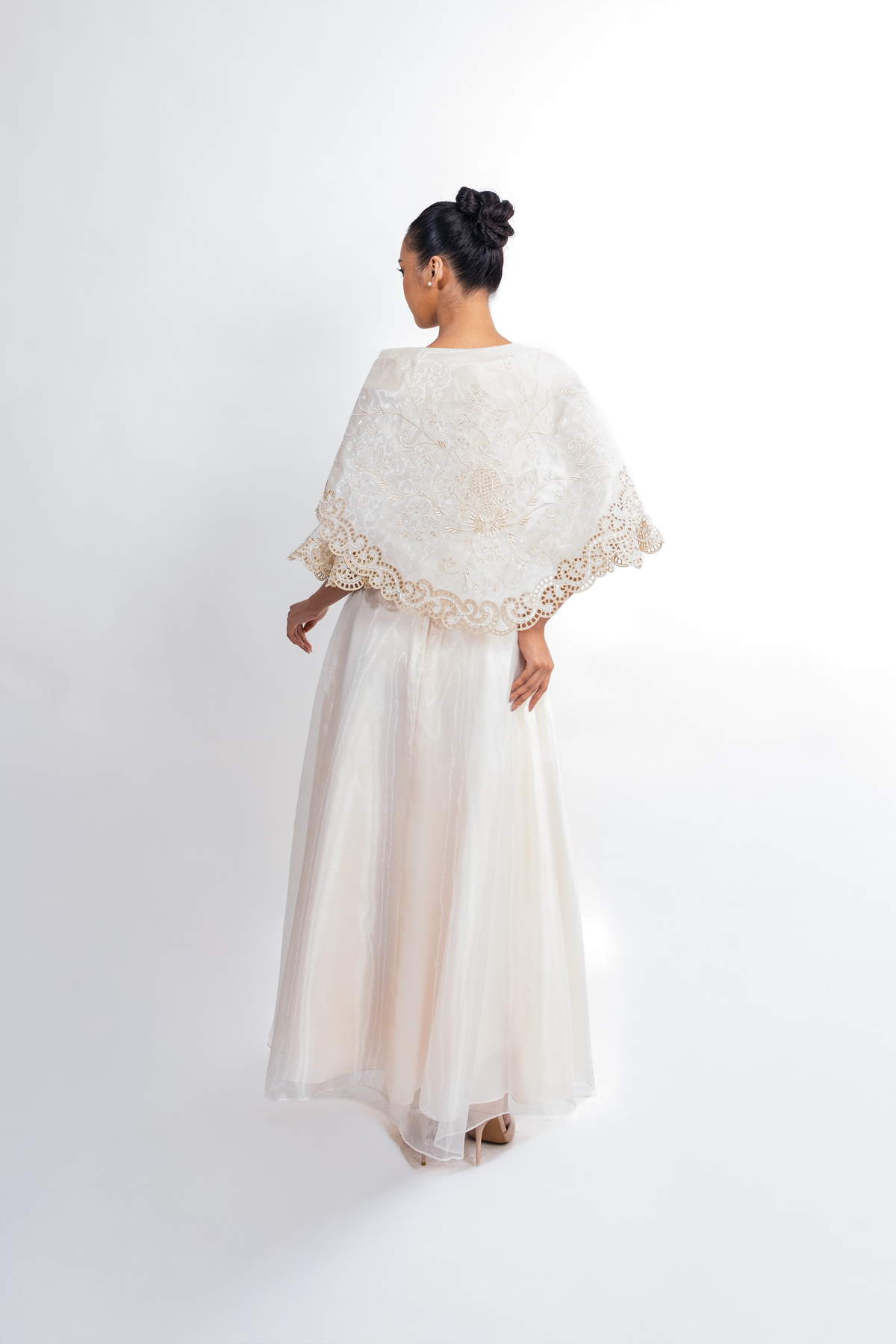 A woman viewed from behind wearing a cream-colored lace alampay with a tulle maxi skirt, set against a plain white studio background.